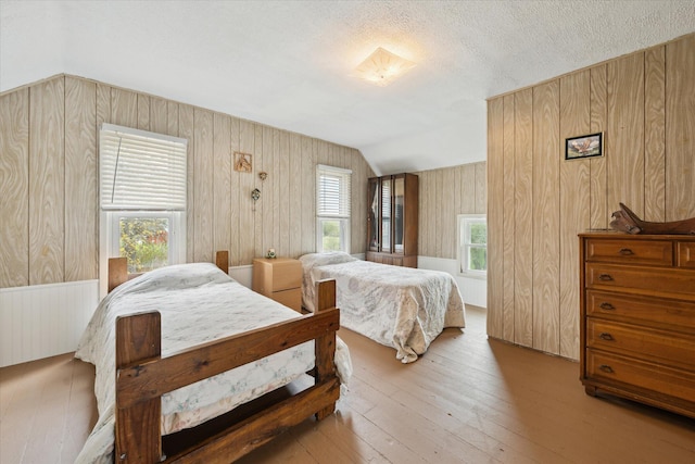 bedroom with a textured ceiling, wood walls, hardwood / wood-style flooring, and vaulted ceiling