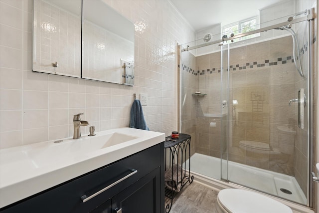 bathroom with wood finished floors, tile walls, toilet, vanity, and a stall shower