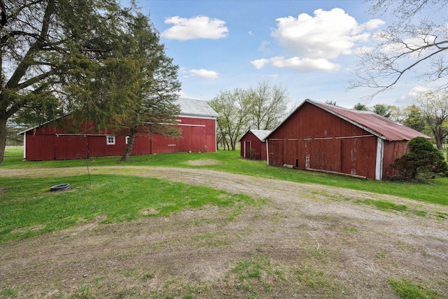 view of pole building with driveway, a lawn, and a barn