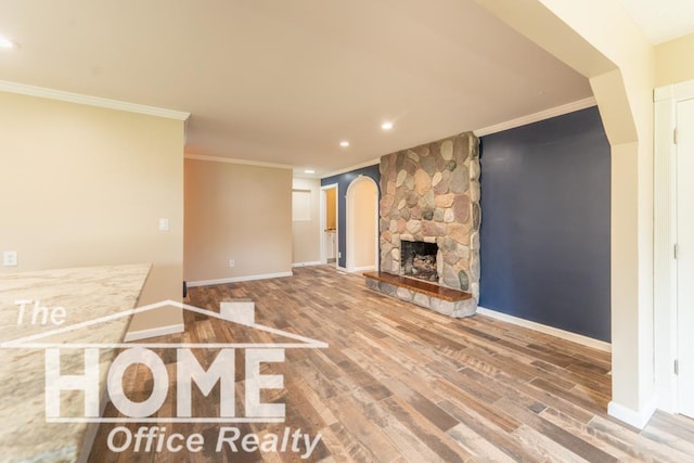 unfurnished living room with crown molding, arched walkways, wood finished floors, and baseboards