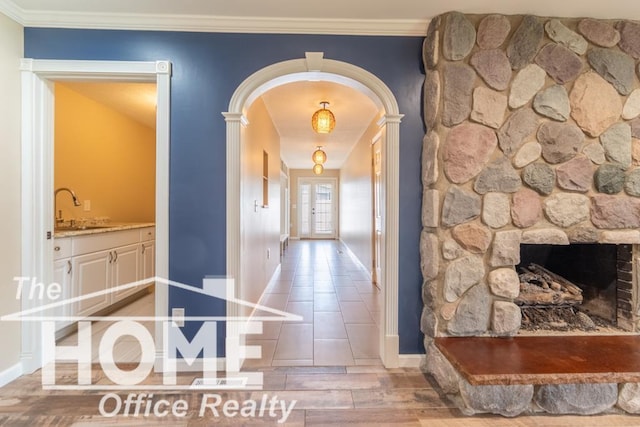 hallway featuring a sink, light wood-style floors, crown molding, baseboards, and arched walkways