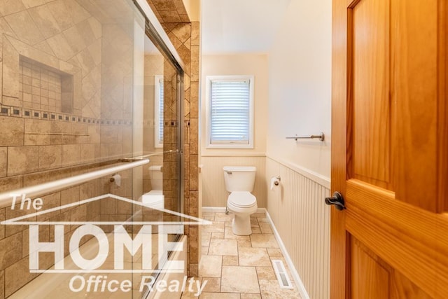 full bathroom with a shower stall, stone finish flooring, toilet, a wainscoted wall, and visible vents