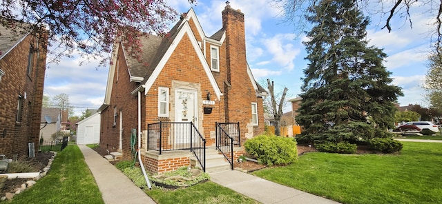 tudor-style house with a chimney, brick siding, a shingled roof, and a front lawn