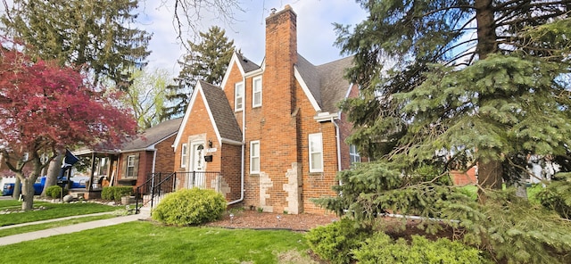 view of side of property featuring a lawn, a chimney, brick siding, and roof with shingles