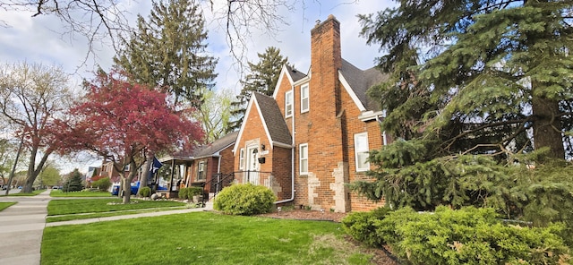 view of side of property with a yard, a shingled roof, a chimney, and brick siding