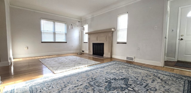unfurnished living room with a fireplace, crown molding, visible vents, baseboards, and wood finished floors