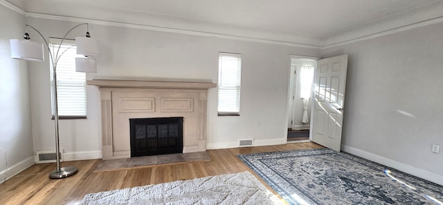 unfurnished living room with a glass covered fireplace, visible vents, wood finished floors, and baseboards