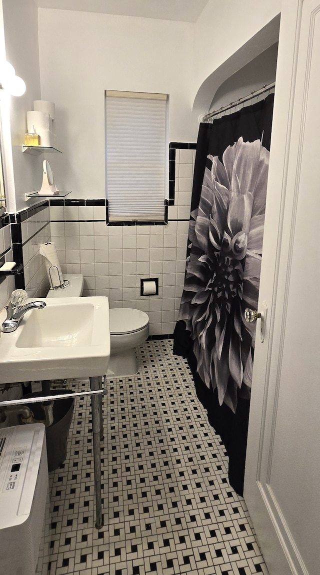 bathroom with a shower with curtain, a sink, toilet, tile walls, and wainscoting