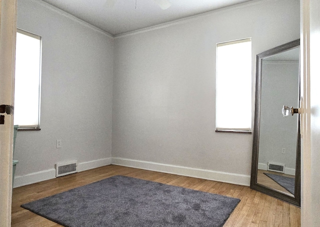 empty room with baseboards, visible vents, ornamental molding, and wood finished floors