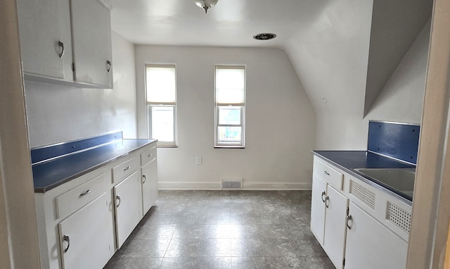 kitchen featuring lofted ceiling, visible vents, white cabinets, and baseboards