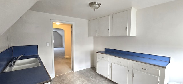 kitchen featuring white cabinetry, baseboards, and a sink