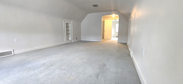 bonus room with lofted ceiling, light colored carpet, visible vents, arched walkways, and built in shelves