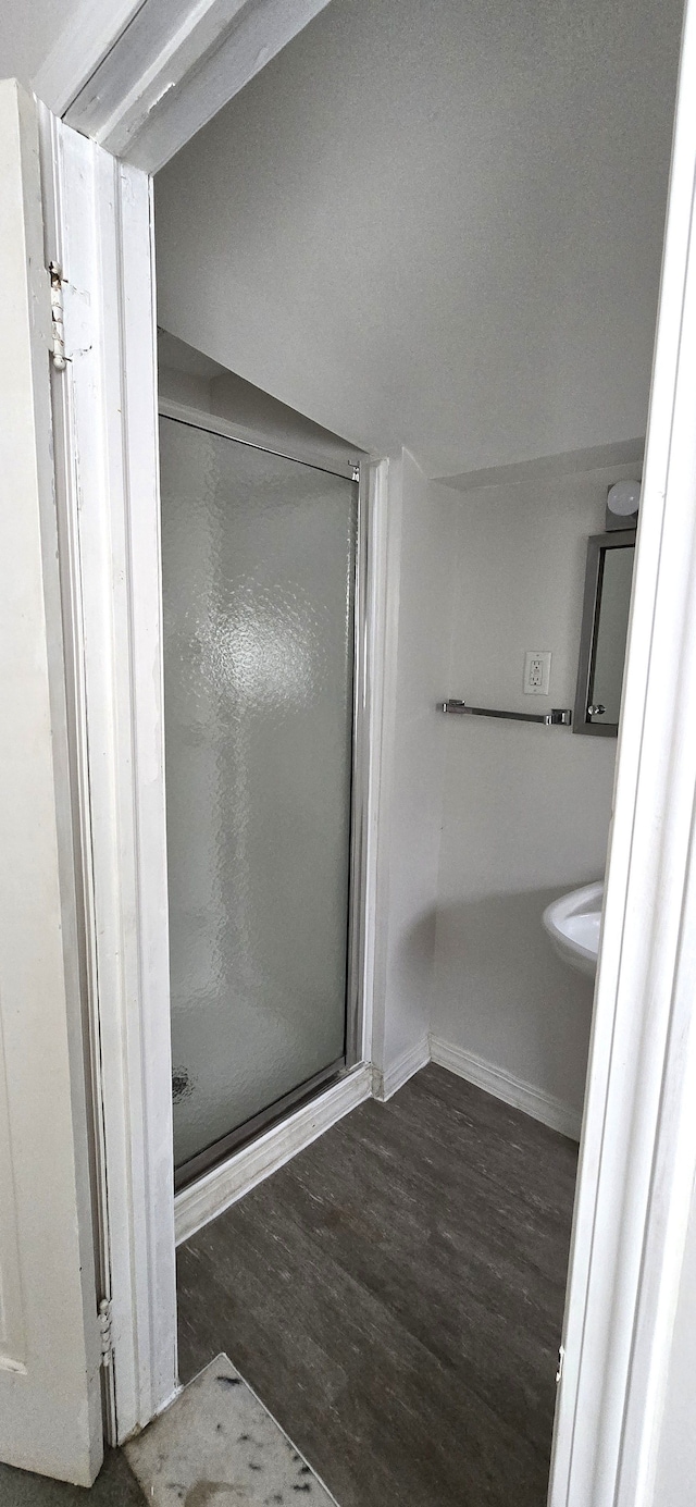 bathroom with baseboards, wood finished floors, and a shower stall