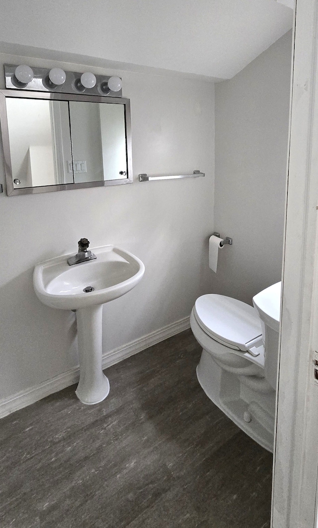 half bathroom with a sink, wood finished floors, toilet, and baseboards