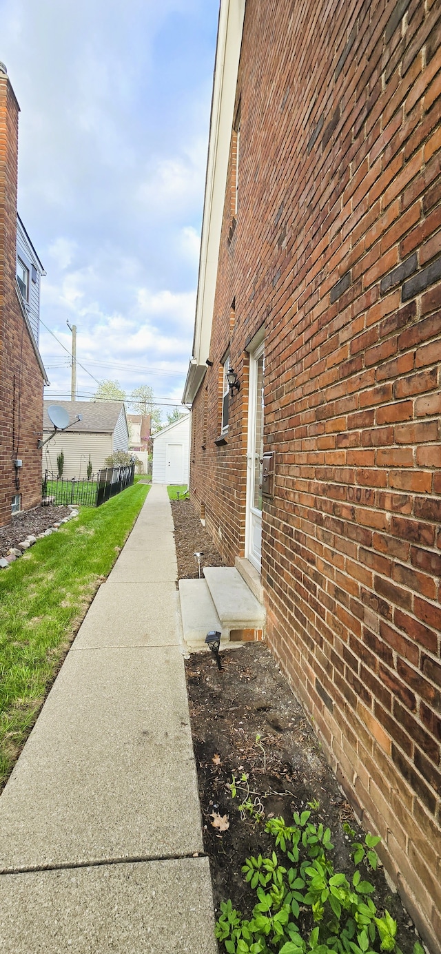 view of property exterior with brick siding, fence, entry steps, and a lawn