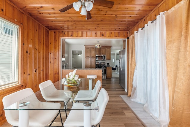 dining area with wooden walls, light wood finished floors, ceiling fan, and a wealth of natural light