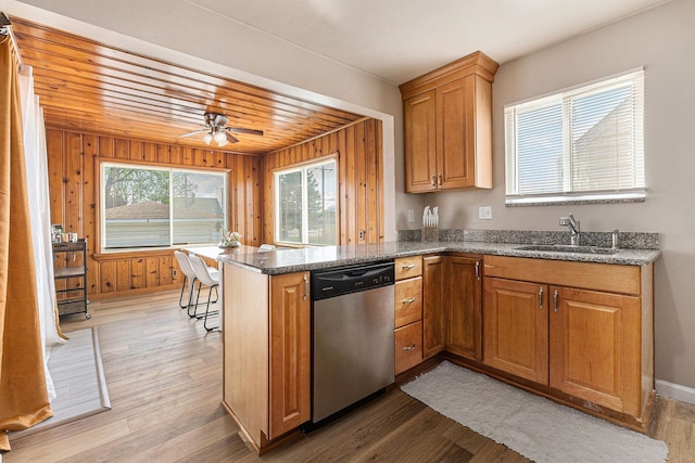 kitchen with dark stone counters, a sink, light wood-type flooring, a peninsula, and dishwasher