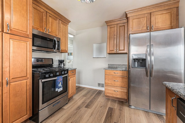 kitchen featuring brown cabinets, dark stone countertops, visible vents, light wood-style flooring, and appliances with stainless steel finishes