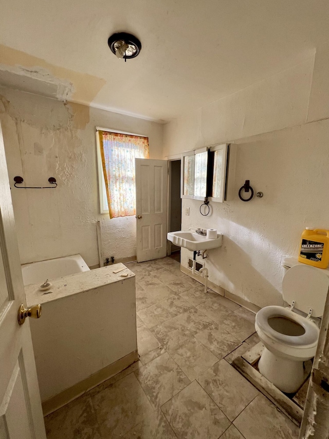 full bathroom featuring a sink, a bathing tub, a textured wall, and toilet
