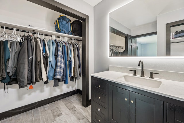 bathroom featuring vanity, baseboards, a walk in closet, and wood finished floors