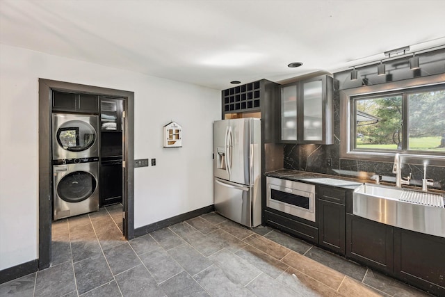 kitchen featuring oven, stacked washer / drying machine, baseboards, backsplash, and stainless steel refrigerator with ice dispenser