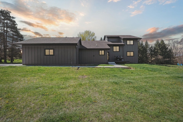 back of house featuring a lawn, board and batten siding, and roof with shingles