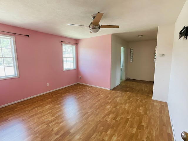 empty room with baseboards, a ceiling fan, and light wood-style flooring