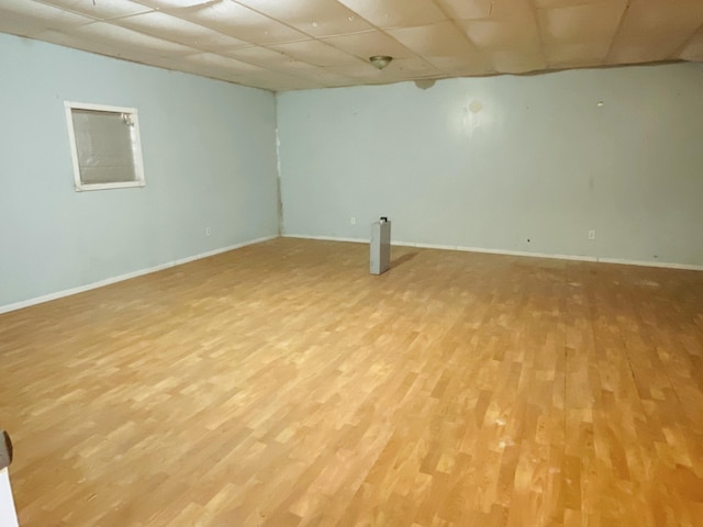 finished below grade area with baseboards, a drop ceiling, and light wood-style flooring