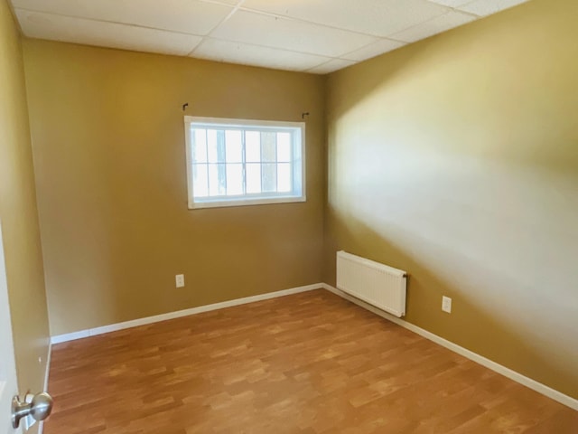 unfurnished room featuring radiator, baseboards, light wood finished floors, and a paneled ceiling