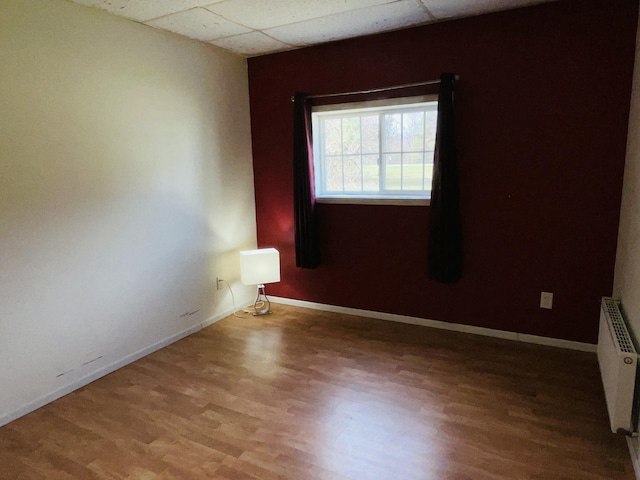 empty room featuring radiator heating unit, baseboards, wood finished floors, and a paneled ceiling