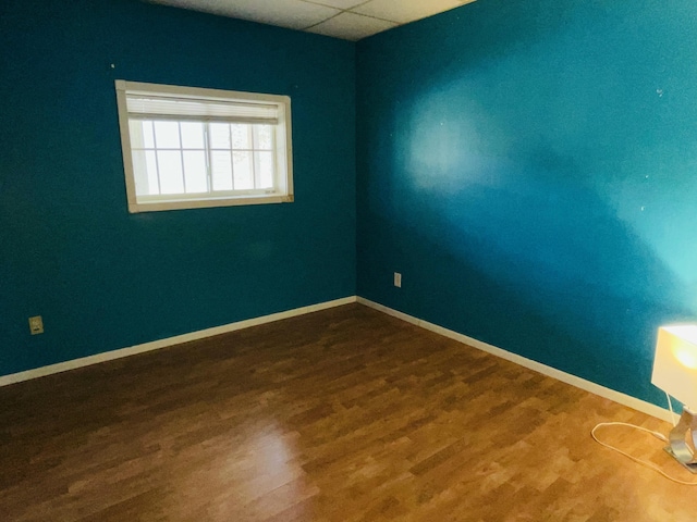 unfurnished room with baseboards, a drop ceiling, and wood finished floors