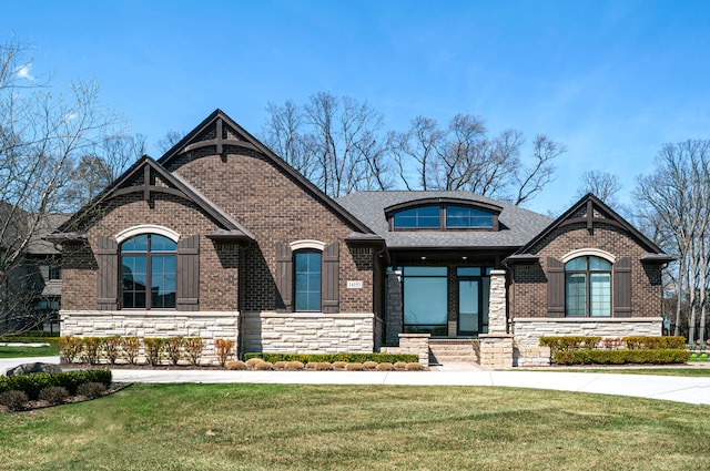 view of front of house featuring brick siding, stone siding, a shingled roof, and a front yard