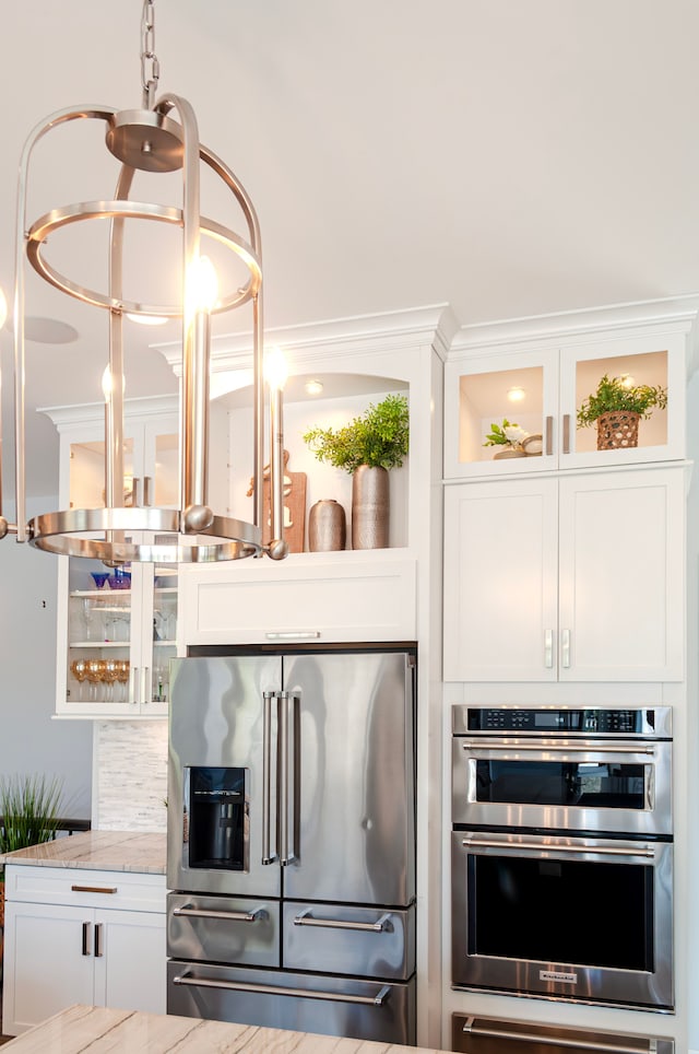 kitchen featuring white cabinetry, light stone countertops, appliances with stainless steel finishes, and glass insert cabinets