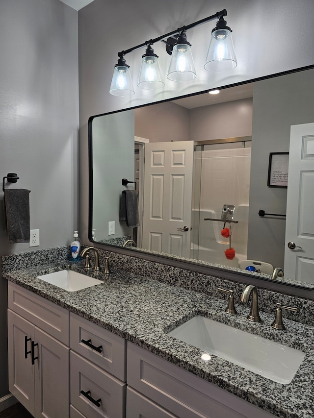bathroom with a shower with shower door, double vanity, and a sink