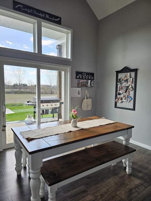 dining room featuring dark wood-type flooring, vaulted ceiling, and baseboards