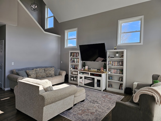 living room with a towering ceiling, an inviting chandelier, dark wood-style flooring, and baseboards