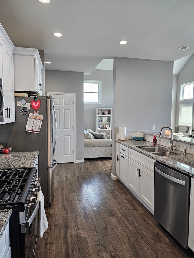 kitchen with light stone counters, a sink, appliances with stainless steel finishes, and dark wood finished floors