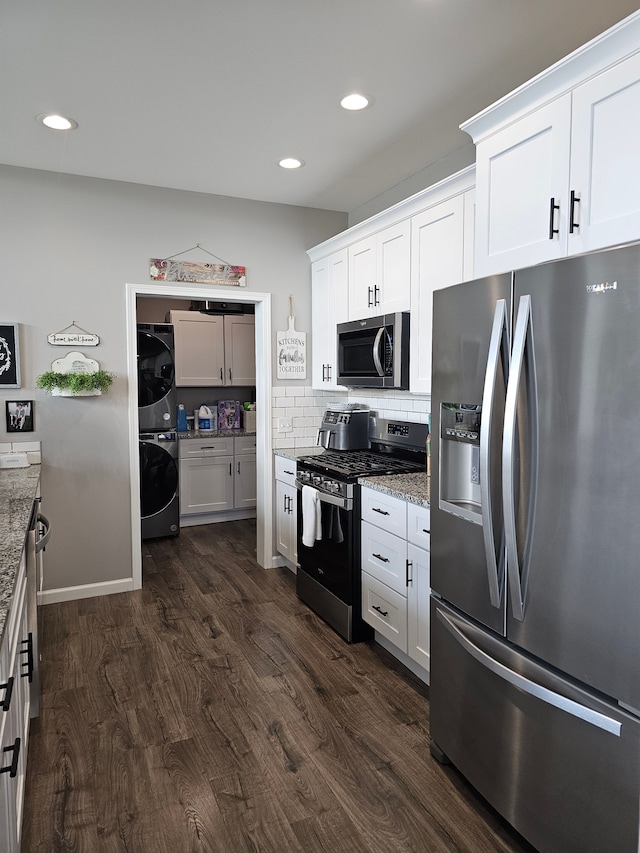kitchen featuring dark wood finished floors, stacked washing maching and dryer, stainless steel appliances, and light stone counters