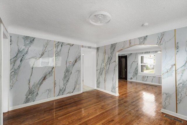 empty room with wood finished floors, visible vents, wallpapered walls, and a textured ceiling