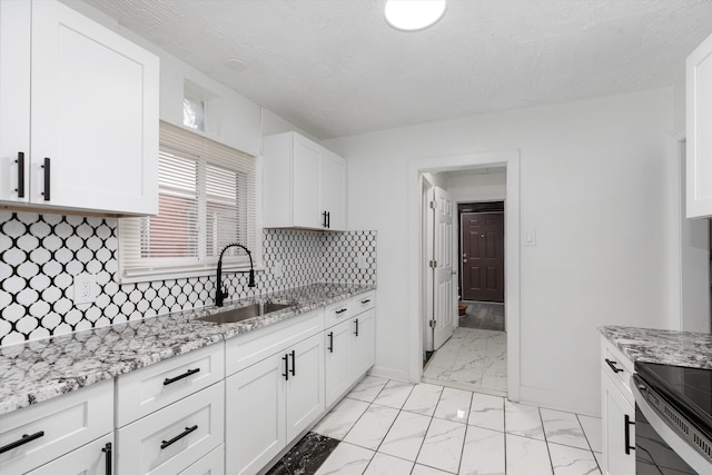 kitchen featuring light stone counters, decorative backsplash, marble finish floor, a sink, and white cabinetry