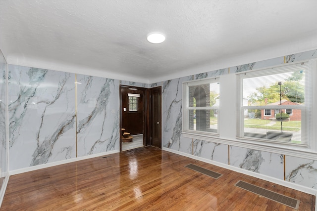 empty room featuring wood finished floors, visible vents, baseboards, and a textured ceiling