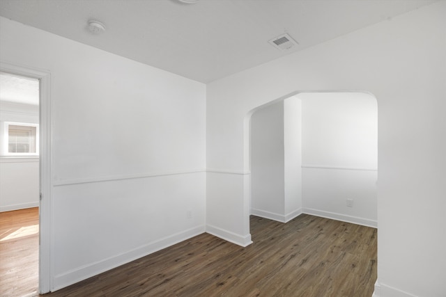 empty room with arched walkways, visible vents, wood finished floors, and baseboards