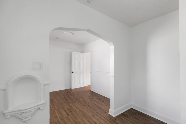 spare room with arched walkways, wood finished floors, and baseboards