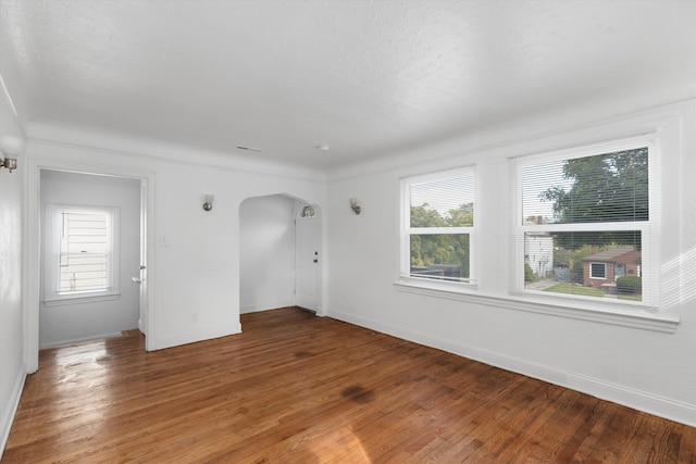 unfurnished room featuring light wood-type flooring, plenty of natural light, baseboards, and arched walkways