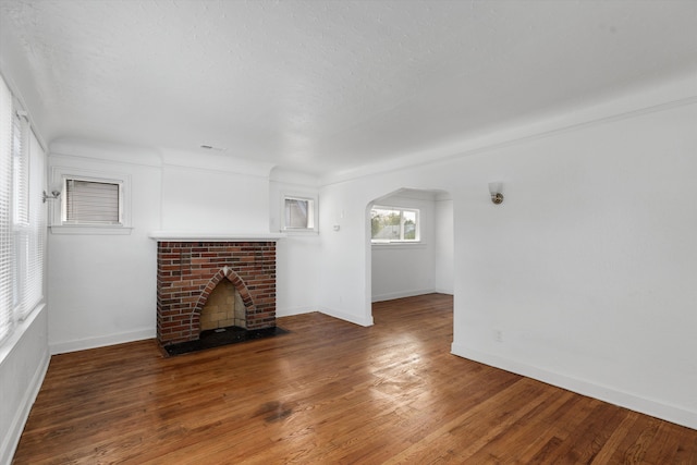 unfurnished living room featuring arched walkways, wood finished floors, a fireplace, baseboards, and visible vents