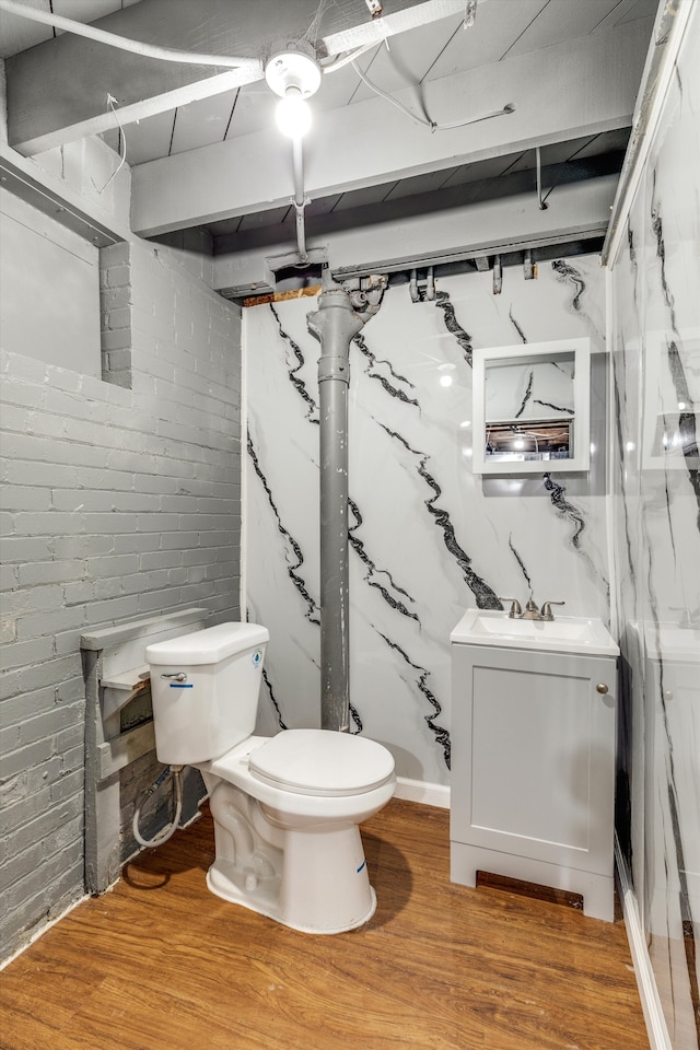 bathroom with wood finished floors, toilet, brick wall, and a sink