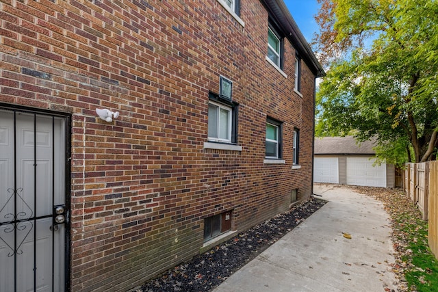 view of side of home featuring an outbuilding, brick siding, a garage, and fence