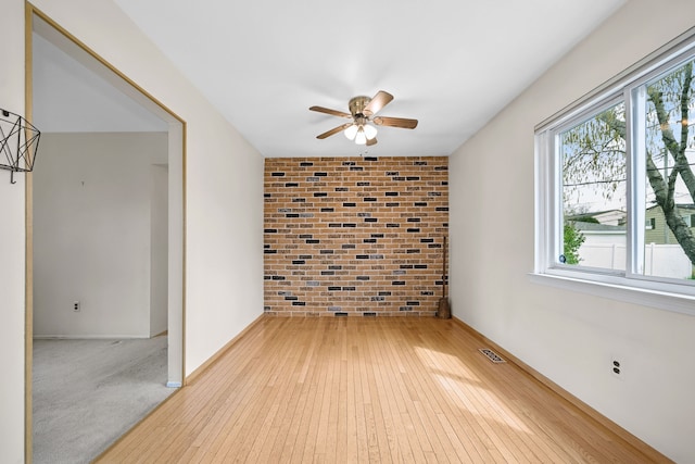 empty room with baseboards, light wood-type flooring, ceiling fan, and brick wall