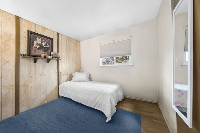 bedroom with wooden walls, wood finished floors, and baseboards