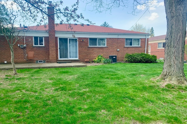 back of house with a lawn, a chimney, a patio area, and brick siding